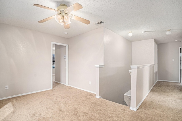 empty room featuring ceiling fan, a textured ceiling, and light carpet