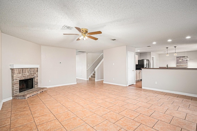 unfurnished living room with ceiling fan, a textured ceiling, light tile patterned floors, and a fireplace