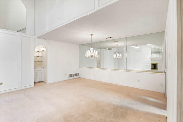 unfurnished room with ceiling fan with notable chandelier, light carpet, and a fireplace