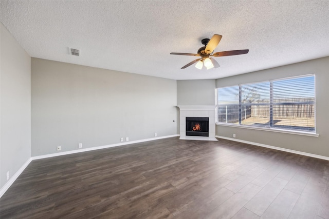 unfurnished living room with ceiling fan, dark wood-type flooring, a textured ceiling, and a tiled fireplace