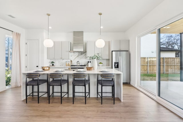 kitchen featuring tasteful backsplash, wall chimney range hood, light wood-type flooring, a breakfast bar area, and stainless steel fridge