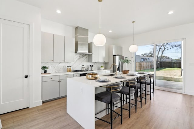 kitchen featuring decorative light fixtures, sink, a kitchen island with sink, wall chimney range hood, and stainless steel appliances