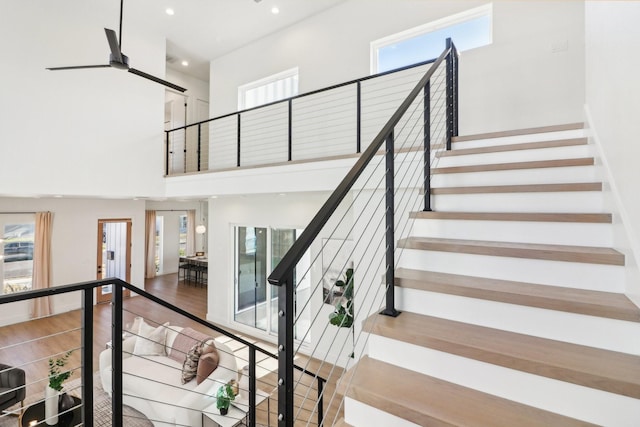 stairs with ceiling fan, a high ceiling, and hardwood / wood-style floors