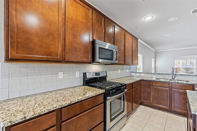 kitchen featuring stainless steel appliances, light tile patterned flooring, a sink, light stone countertops, and plenty of natural light