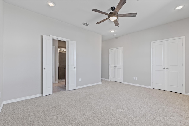 unfurnished bedroom featuring light carpet, recessed lighting, visible vents, and multiple closets