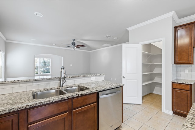 kitchen with light tile patterned floors, decorative backsplash, stainless steel dishwasher, a sink, and light stone countertops