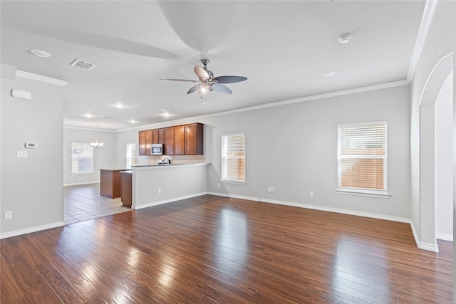 unfurnished living room featuring baseboards, ornamental molding, dark wood-type flooring, and ceiling fan with notable chandelier