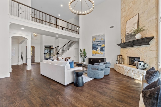 living room with a towering ceiling, an inviting chandelier, a fireplace, and dark wood-type flooring