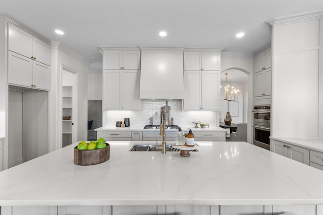 kitchen featuring backsplash, custom exhaust hood, light stone countertops, and a spacious island