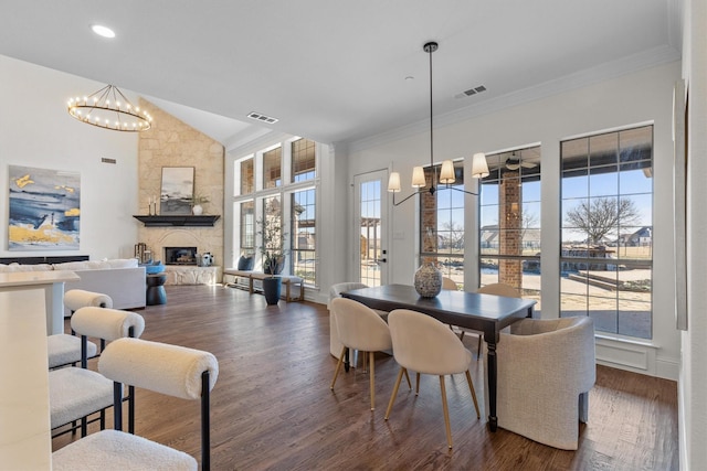 dining area featuring dark hardwood / wood-style floors, plenty of natural light, a stone fireplace, and a notable chandelier