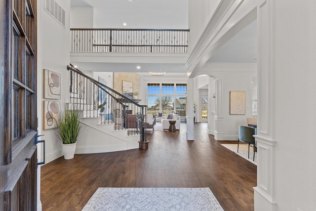 foyer entrance featuring ornamental molding, dark hardwood / wood-style flooring, decorative columns, and a high ceiling