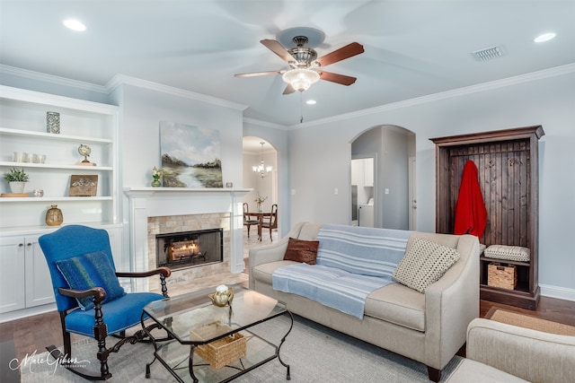 living room featuring crown molding, a tile fireplace, hardwood / wood-style flooring, and ceiling fan with notable chandelier