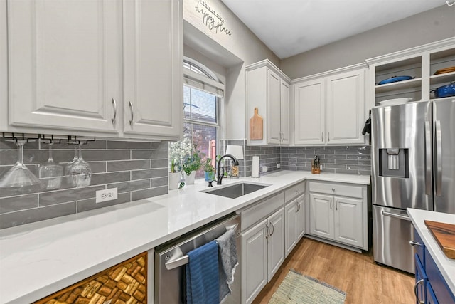 kitchen featuring white cabinetry, sink, light hardwood / wood-style flooring, backsplash, and stainless steel appliances