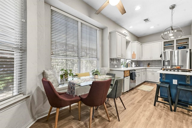 kitchen featuring tasteful backsplash, hanging light fixtures, white cabinets, light hardwood / wood-style flooring, and stainless steel appliances