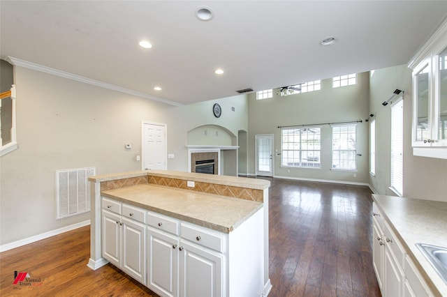 kitchen featuring dark hardwood / wood-style flooring, sink, a tiled fireplace, white cabinets, and a center island