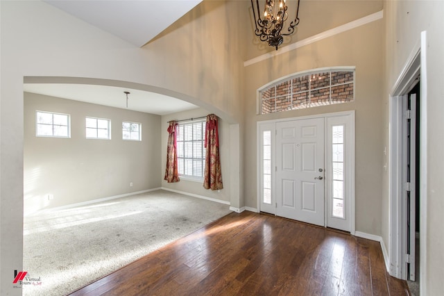 entryway with dark wood-type flooring, a towering ceiling, and an inviting chandelier