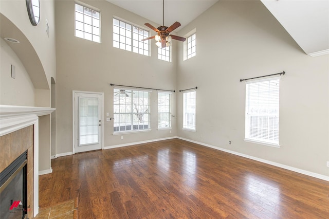 unfurnished living room featuring a towering ceiling, ceiling fan, dark hardwood / wood-style floors, and a fireplace