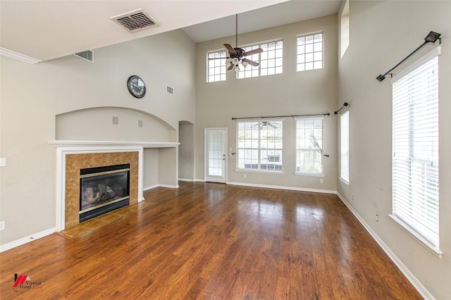 unfurnished living room featuring ceiling fan, dark hardwood / wood-style flooring, a towering ceiling, and a fireplace