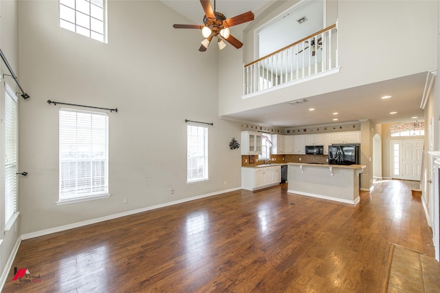 unfurnished living room with a high ceiling, plenty of natural light, and dark wood-type flooring