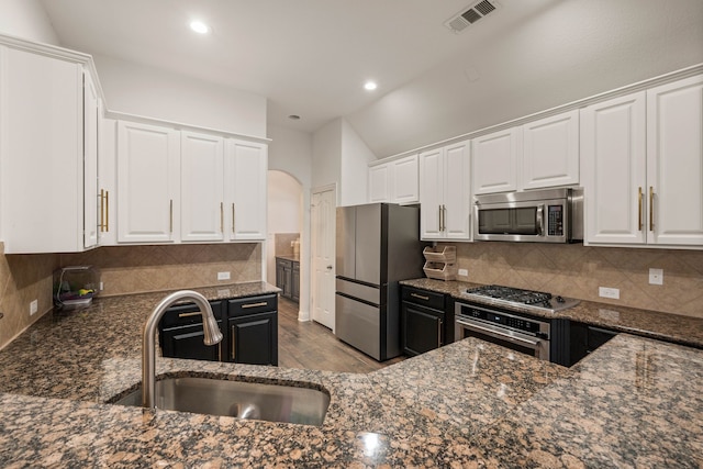 kitchen with appliances with stainless steel finishes, sink, dark stone countertops, white cabinets, and decorative backsplash