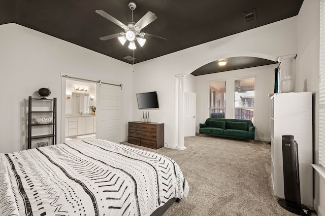 bedroom featuring ceiling fan, ensuite bathroom, carpet floors, a barn door, and ornate columns