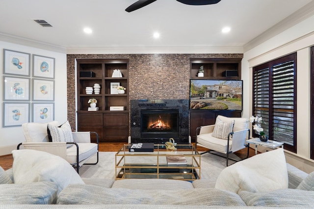 living room with crown molding, light hardwood / wood-style flooring, built in features, ceiling fan, and a tiled fireplace