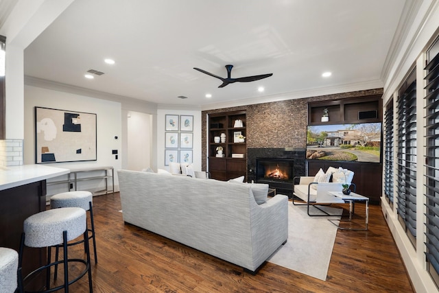 living room with dark wood-type flooring, built in shelves, ornamental molding, and a fireplace