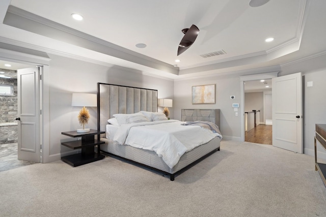 bedroom featuring ornamental molding, ensuite bathroom, a tray ceiling, and carpet