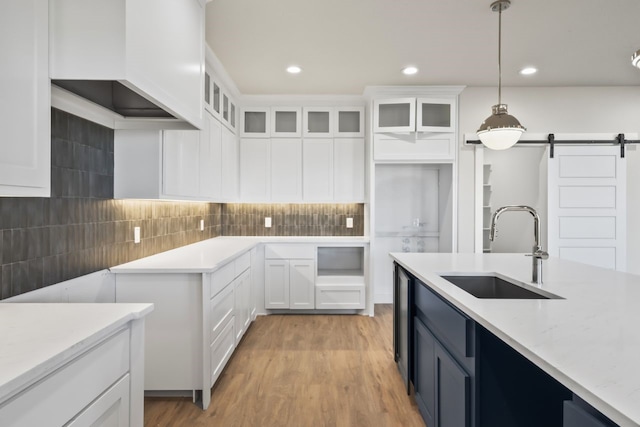 kitchen with light stone countertops, white cabinetry, a barn door, hanging light fixtures, and sink