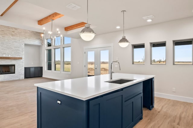 kitchen with hanging light fixtures, sink, blue cabinetry, beam ceiling, and a kitchen island with sink