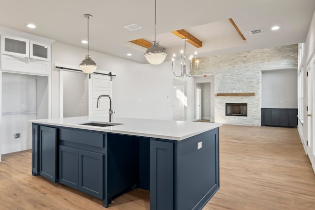 kitchen with beamed ceiling, a barn door, white cabinets, blue cabinets, and a center island with sink