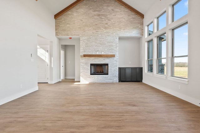 unfurnished living room with a high ceiling, light hardwood / wood-style flooring, beam ceiling, and a fireplace