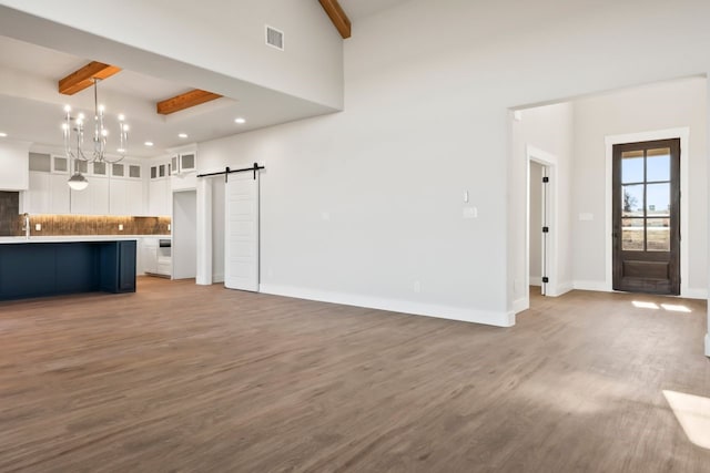 unfurnished living room featuring sink, beamed ceiling, a barn door, and hardwood / wood-style floors