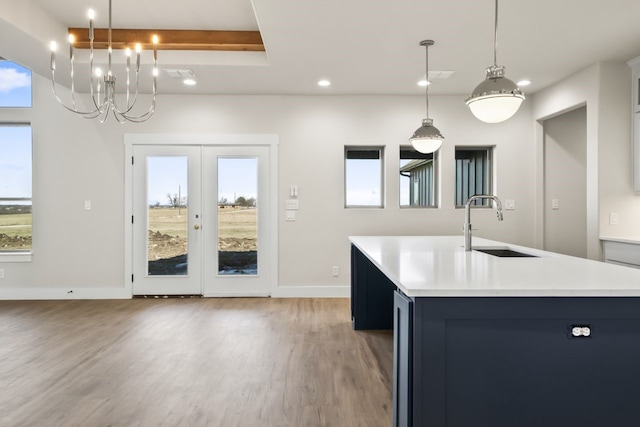 kitchen featuring french doors, an island with sink, sink, hanging light fixtures, and light wood-type flooring