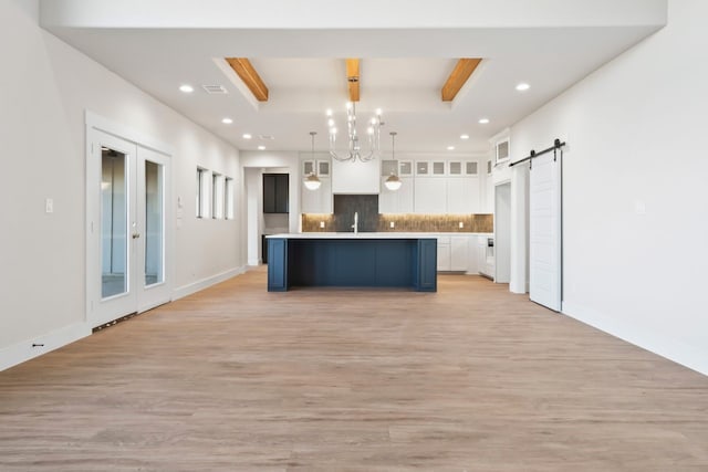 kitchen featuring pendant lighting, white cabinets, an island with sink, light hardwood / wood-style flooring, and a barn door