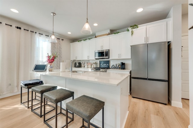 kitchen featuring appliances with stainless steel finishes, sink, decorative light fixtures, white cabinetry, and a kitchen island with sink