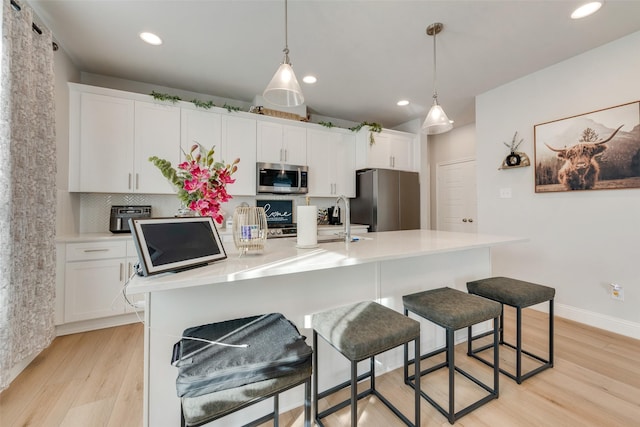 kitchen with white cabinets, an island with sink, hanging light fixtures, and appliances with stainless steel finishes