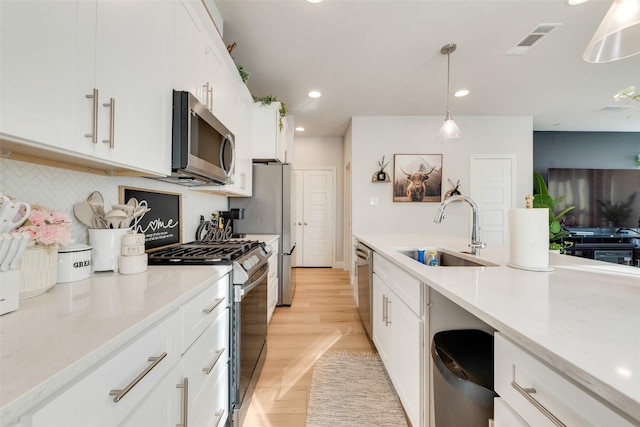 kitchen featuring sink, white cabinets, decorative light fixtures, and appliances with stainless steel finishes