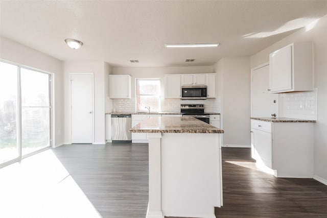 kitchen featuring stone counters, appliances with stainless steel finishes, white cabinetry, a kitchen island, and backsplash