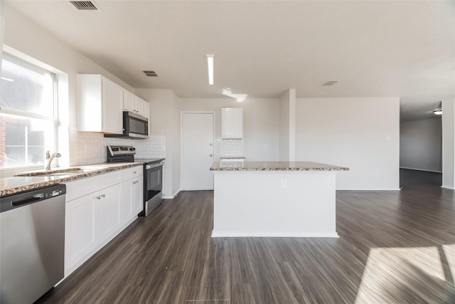 kitchen with appliances with stainless steel finishes, sink, white cabinetry, light stone countertops, and a kitchen island