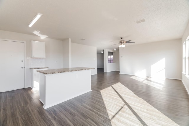 kitchen featuring dark hardwood / wood-style flooring, white cabinets, light stone counters, a center island, and decorative backsplash