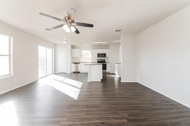 unfurnished living room featuring ceiling fan, a healthy amount of sunlight, and dark hardwood / wood-style floors