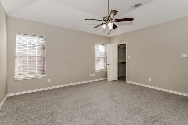 unfurnished bedroom featuring a walk in closet, ceiling fan, carpet flooring, and vaulted ceiling