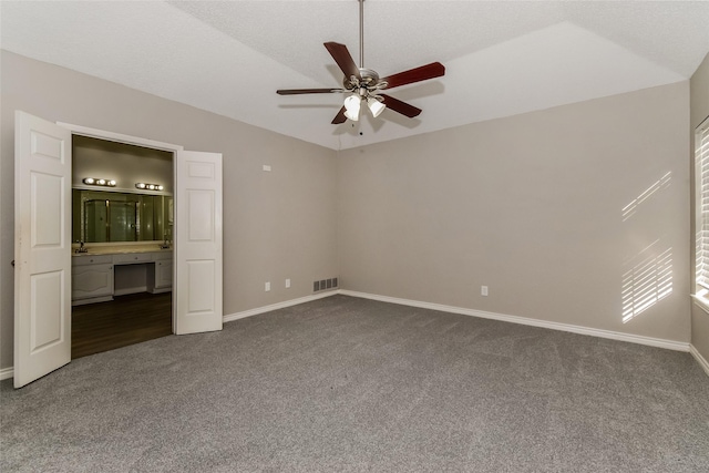 unfurnished bedroom featuring ensuite bathroom, vaulted ceiling, a textured ceiling, carpet, and ceiling fan