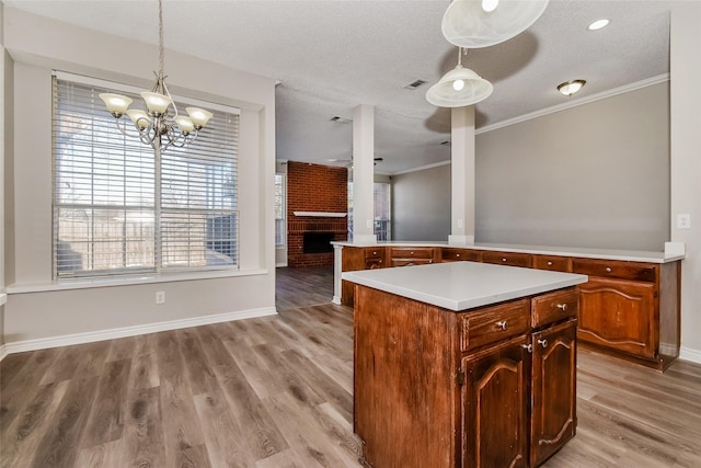 kitchen with hanging light fixtures, a brick fireplace, a textured ceiling, a kitchen island, and light hardwood / wood-style floors