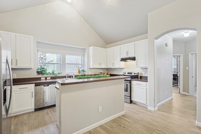 kitchen featuring arched walkways, dark countertops, appliances with stainless steel finishes, under cabinet range hood, and a sink