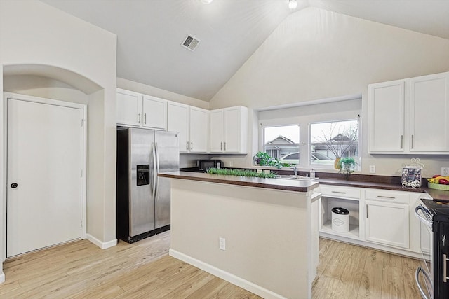 kitchen with appliances with stainless steel finishes, high vaulted ceiling, white cabinets, a center island, and light hardwood / wood-style floors