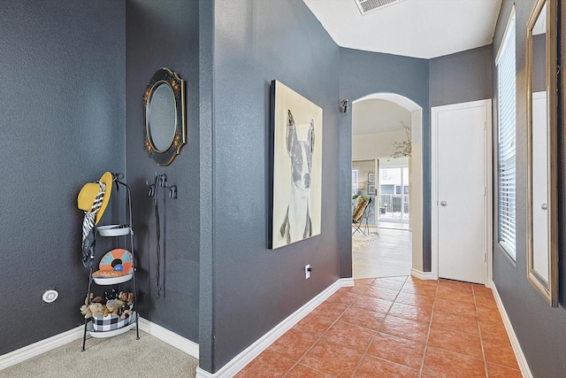 hallway featuring arched walkways, tile patterned flooring, visible vents, and baseboards