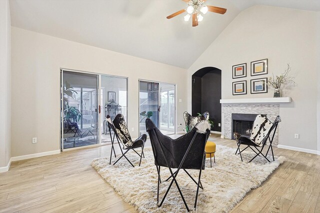 living room featuring ceiling fan, high vaulted ceiling, a fireplace, and light hardwood / wood-style floors