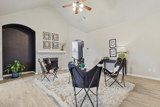 living area featuring arched walkways, a fireplace, visible vents, wood finished floors, and baseboards